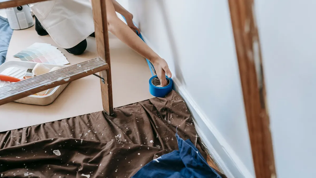 Painter applying masking tape along trim before painting